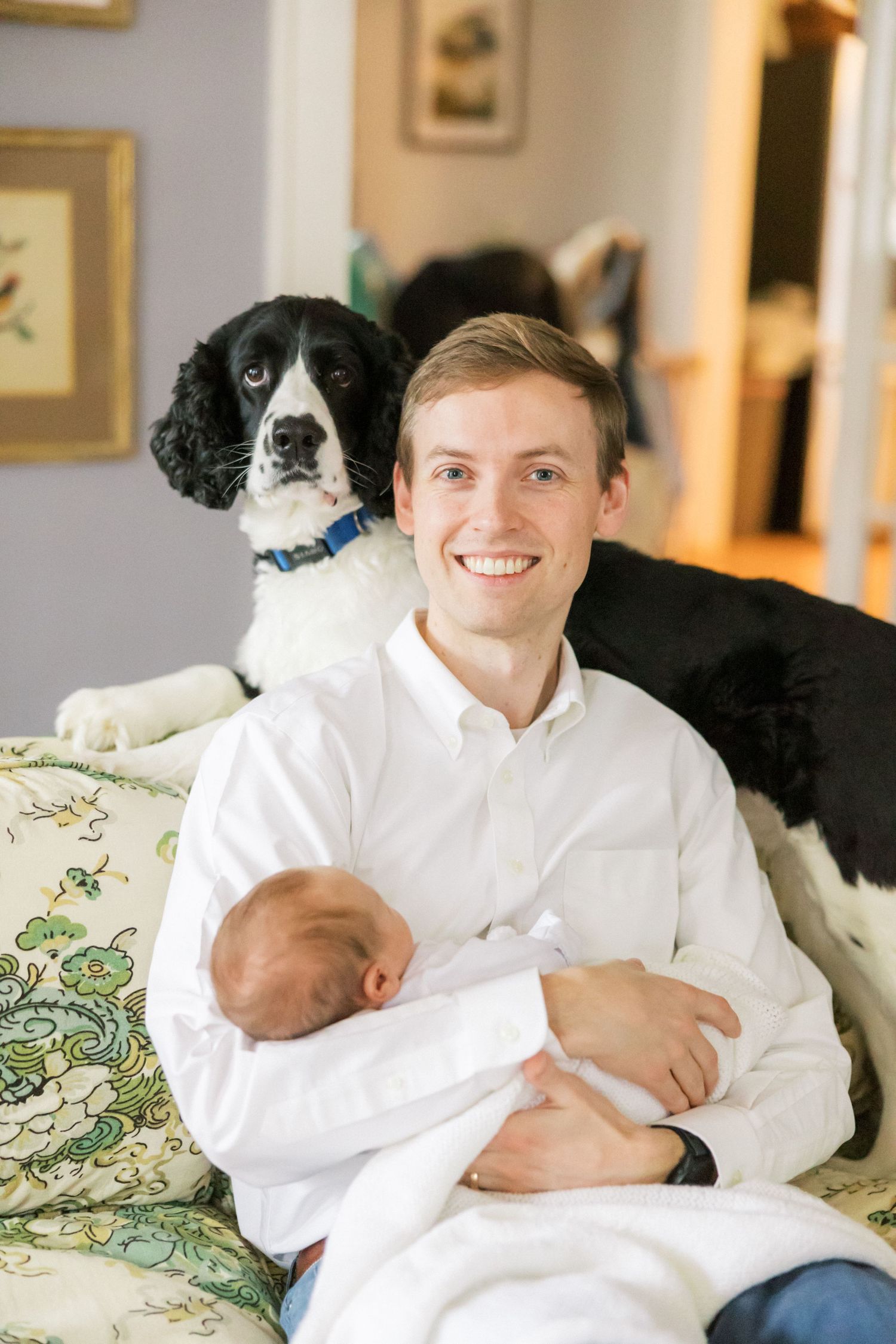 Black and white English Springer Spaniel dog poses with family member holding baby on floral couch.