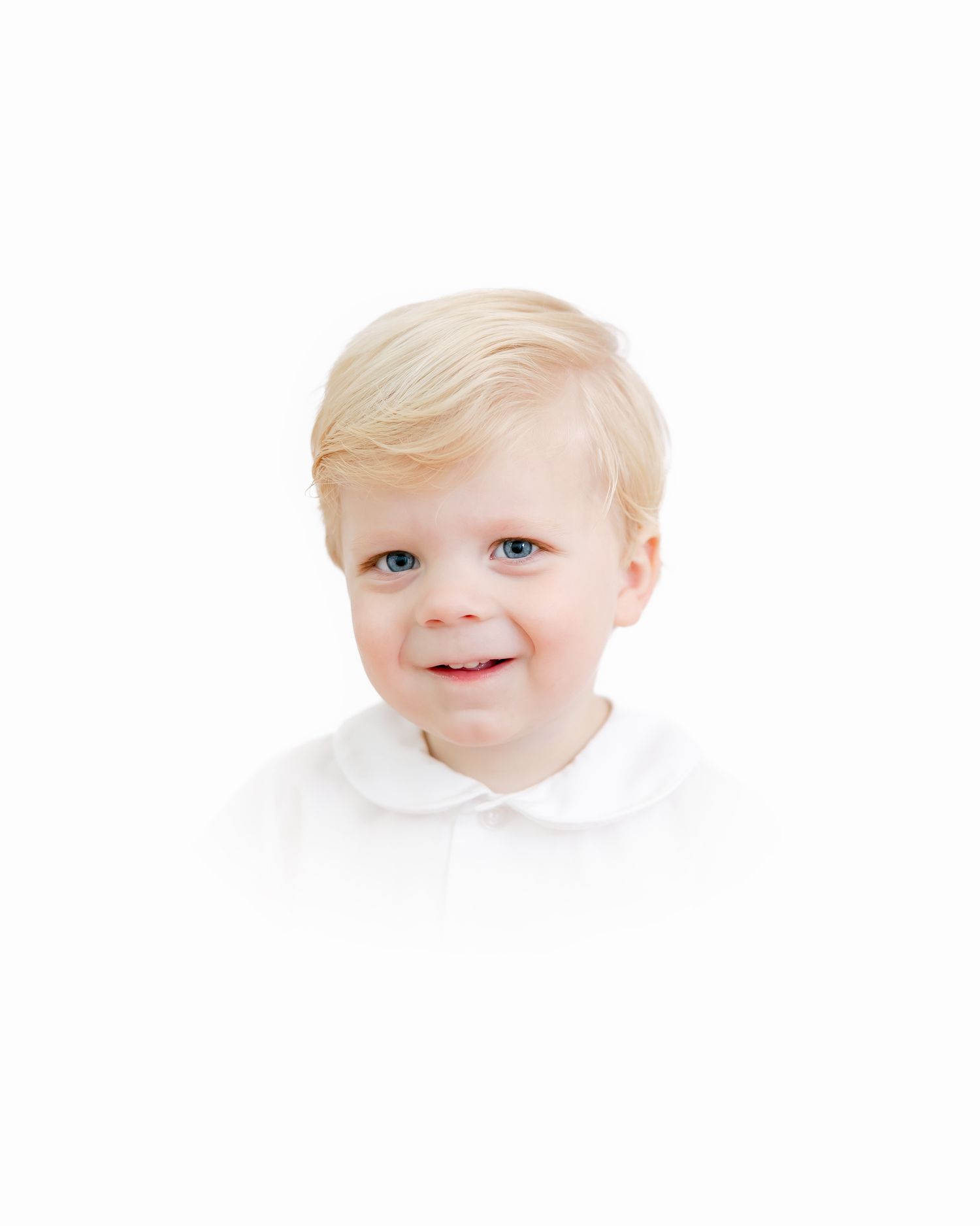 A child with light blond hair and bright blue eyes smiles at the camera against a white background.