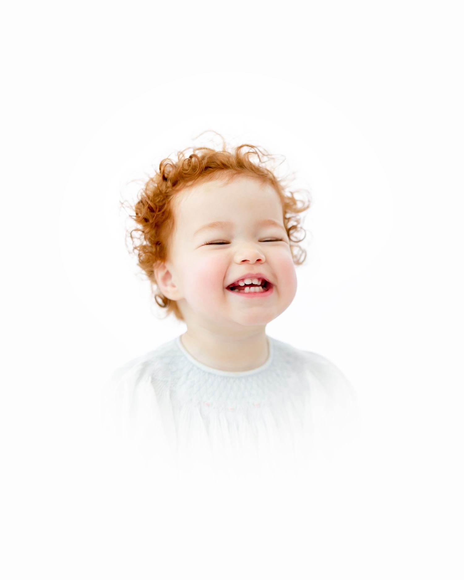A joyful little one with curly ginger hair and a pure white shirt laughs with pure delight.