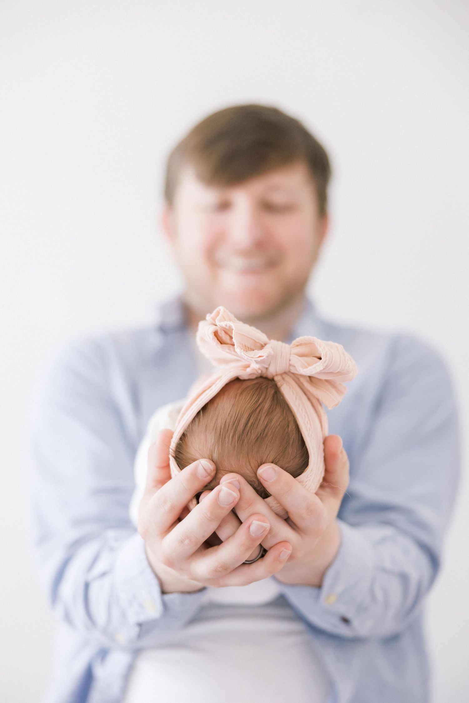 Adult holds sleeping infant wearing pink bow during professional photo session.