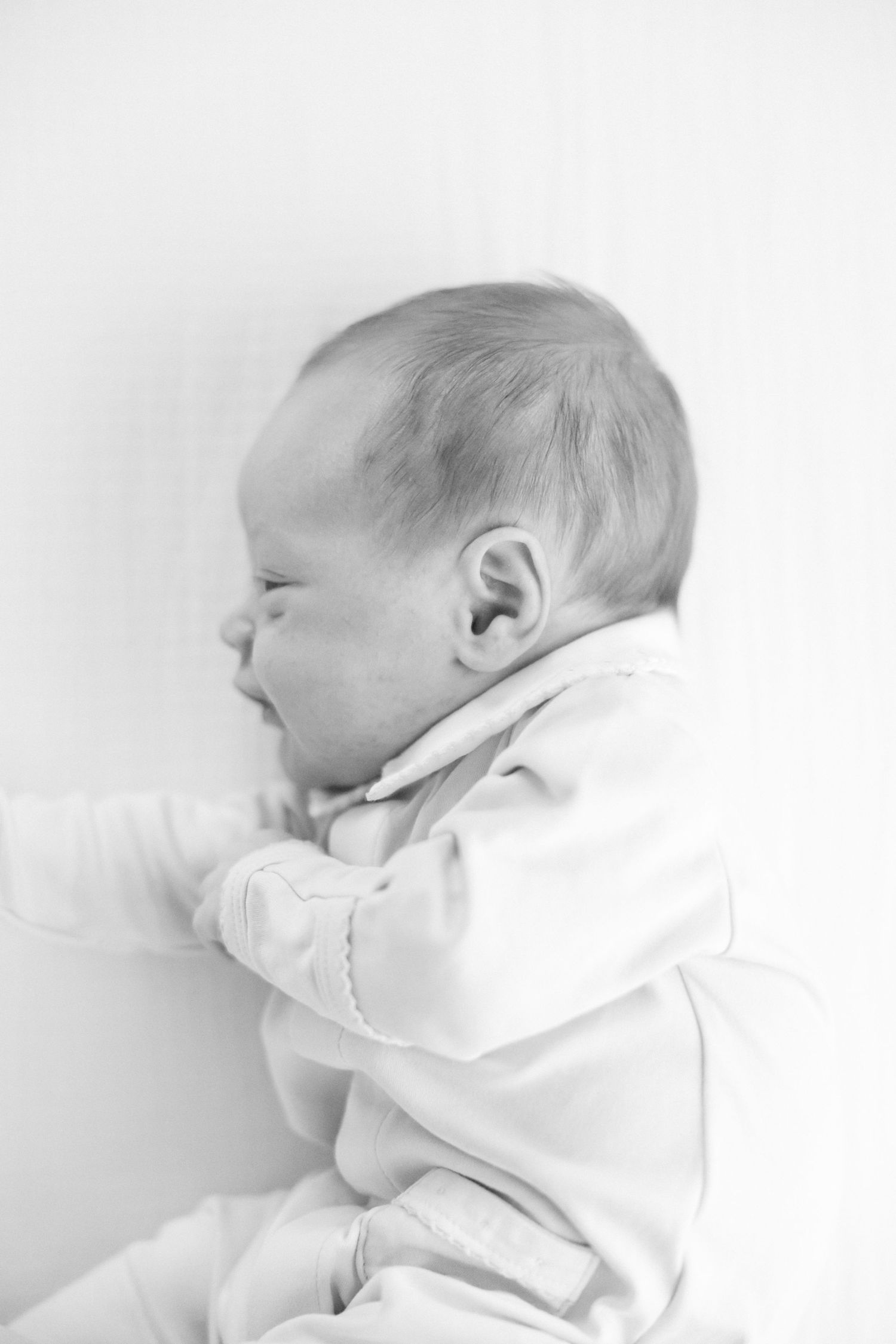 Black and white portrait of a peaceful sleeping newborn in white clothing.