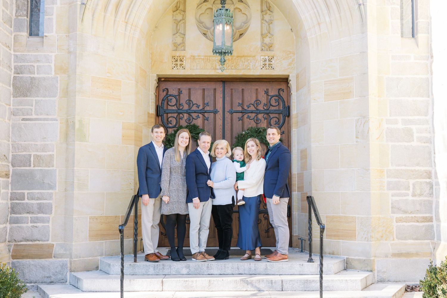 A group stands on stone church steps in front of ornate wooden doors with an arched entryway.