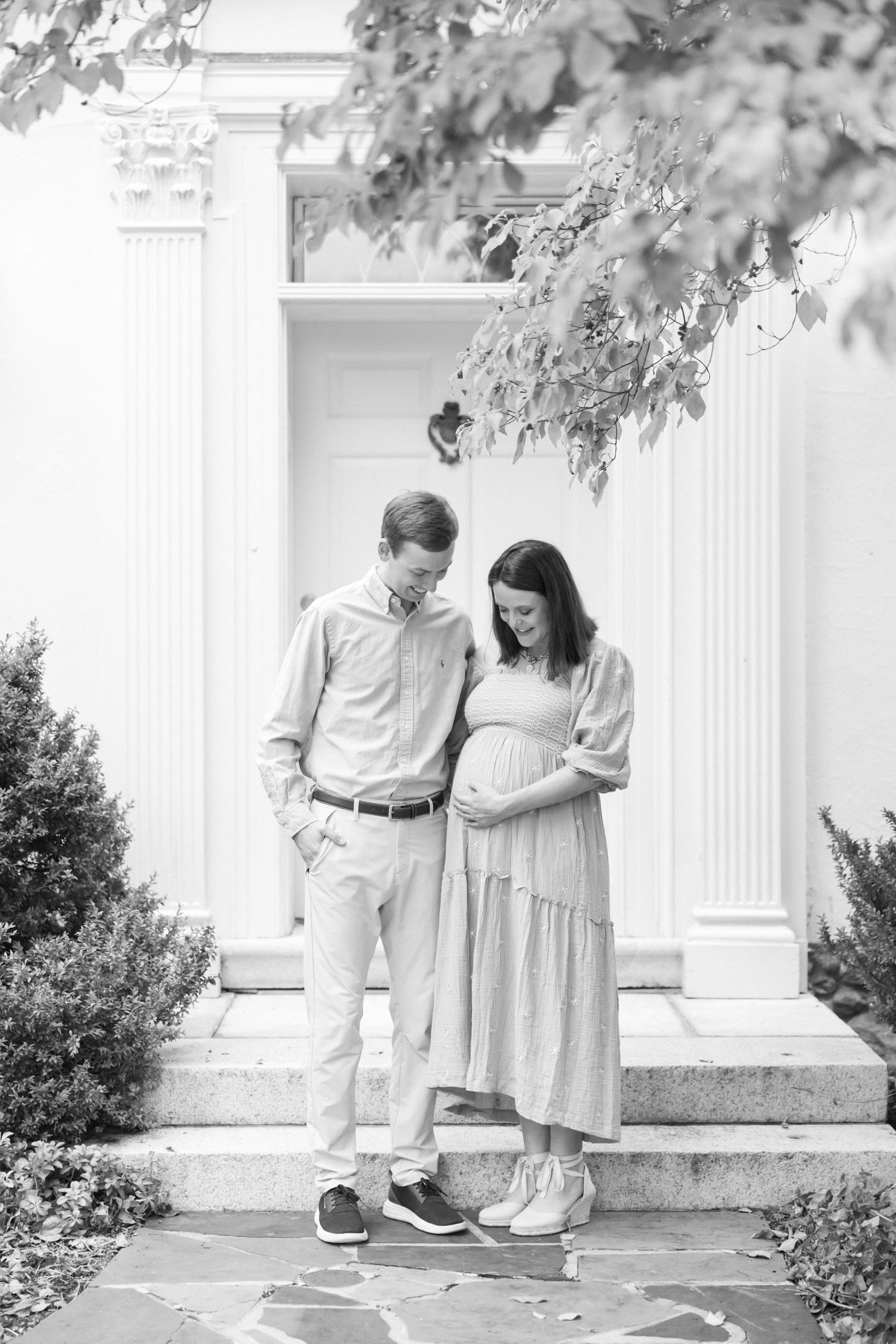 A couple stands together on stone steps outside a white columned entrance in a black and white photograph.