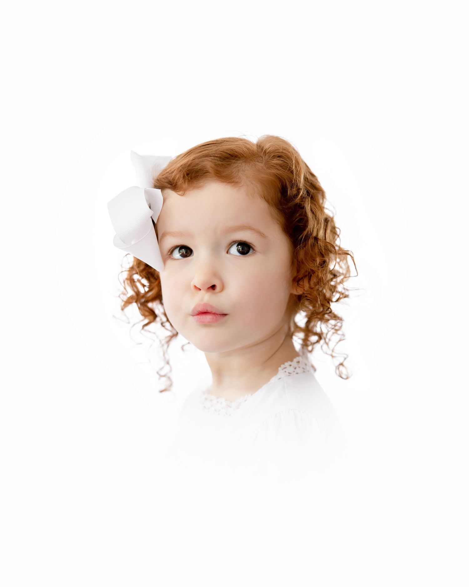 A child with ginger curly hair and a white bow wearing a white top against a white background.