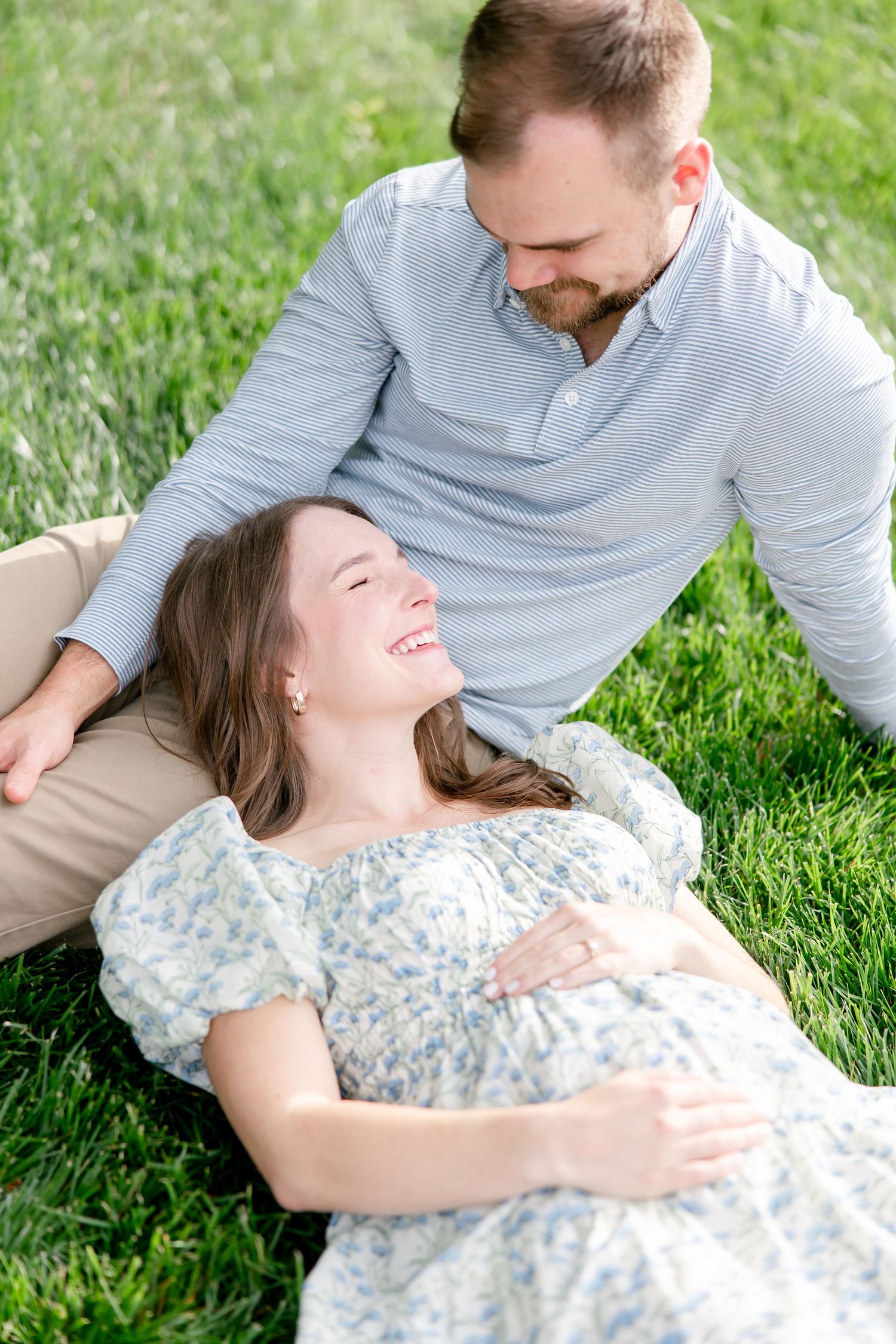 Couple relaxes together on green grass in springtime, wearing casual attire and sharing a tender moment outdoors.
