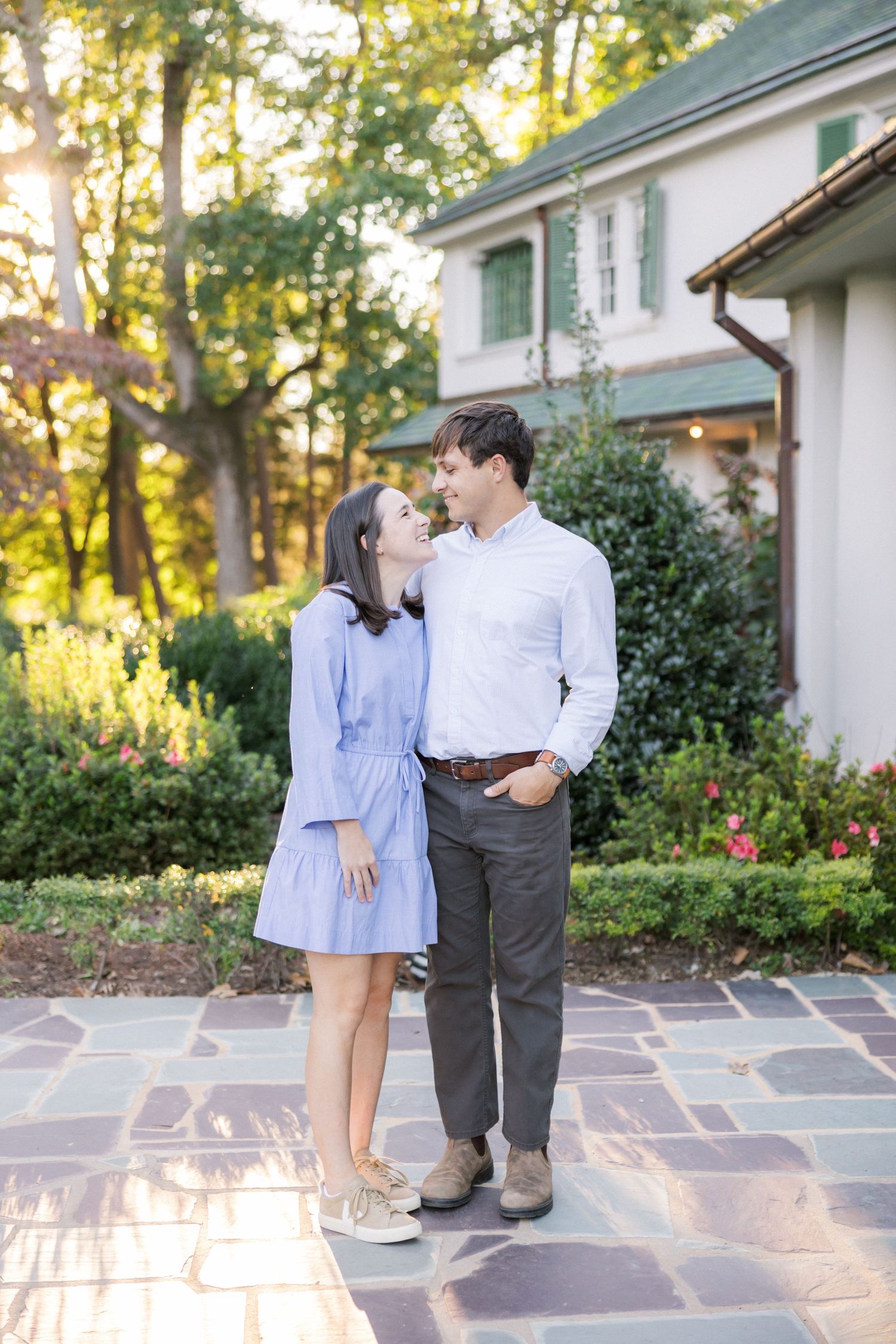 A couple poses together on stone pavement with golden sunlight filtering through trees behind them.