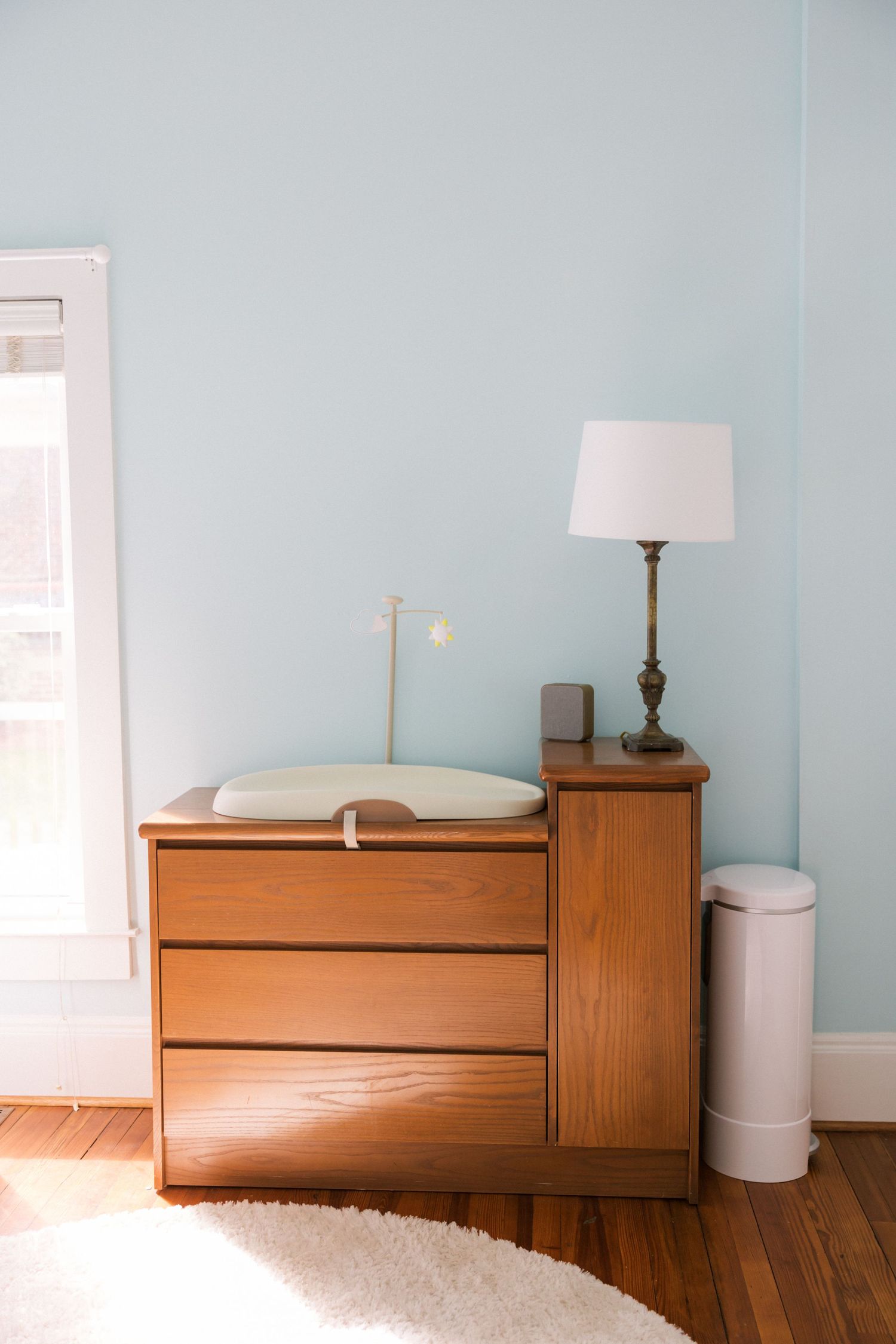 Wooden changing table with white pad and lamp against light blue nursery wall.
