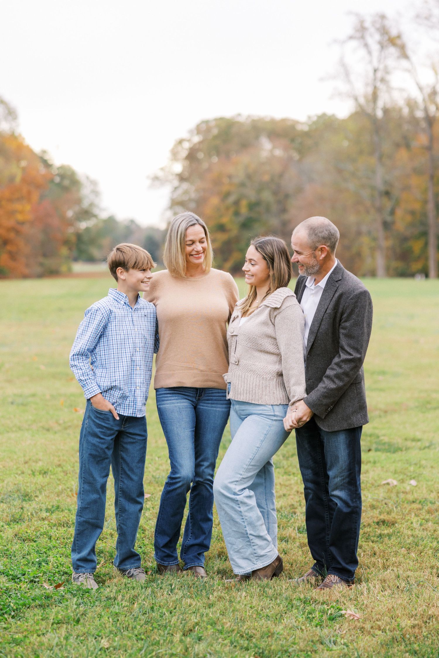 Family poses together in an autumn field with colorful fall foliage in the background.