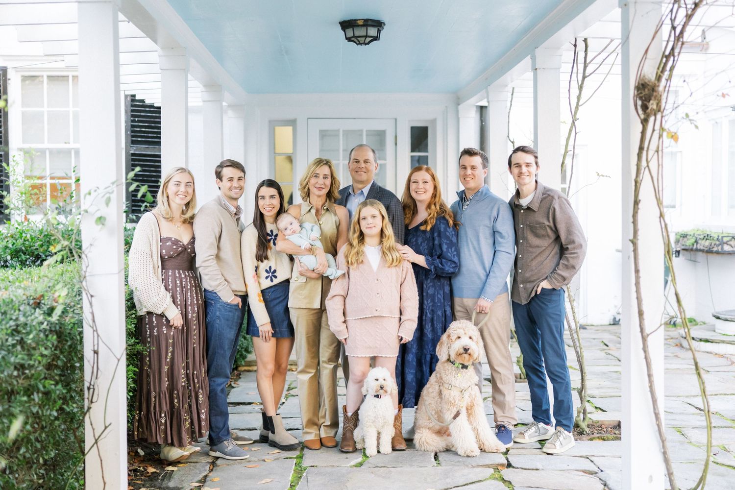 A group stands together with two golden retriever dogs on a covered porch with a light blue ceiling.