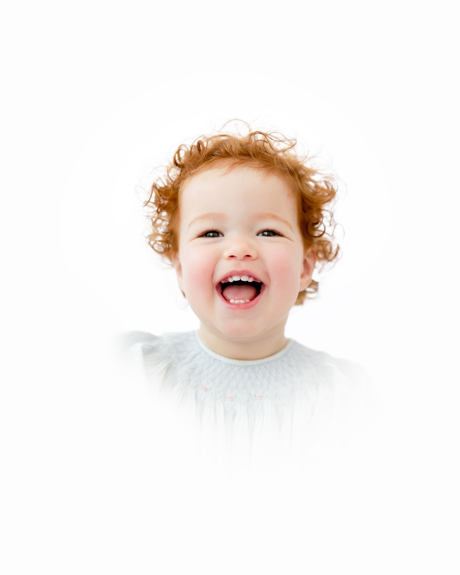 A toddler with curly red hair laughs joyfully against a white background.