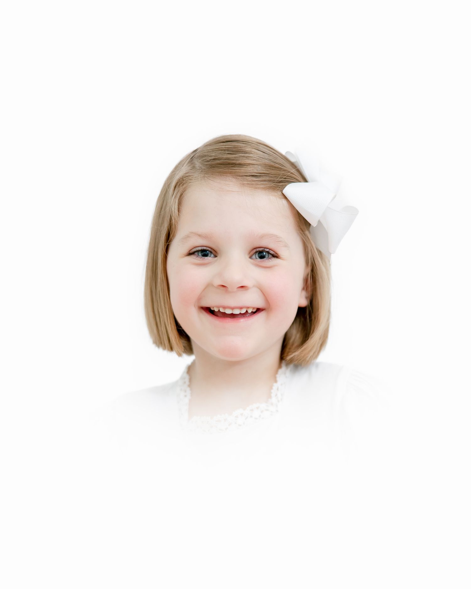 Portrait of a child with a white bow in their short blonde hair wearing a white top against a white background, smiling warmly.