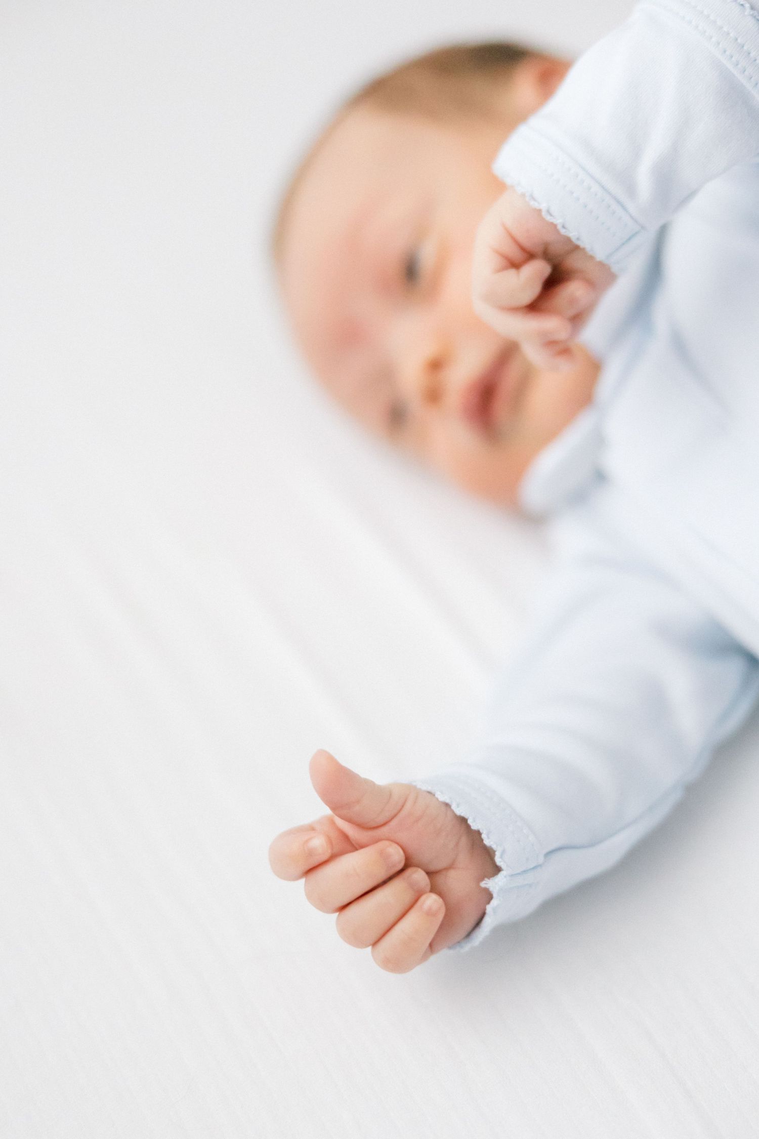 Close-up of a sleeping baby's tiny hand in soft focus wearing light blue clothing.
