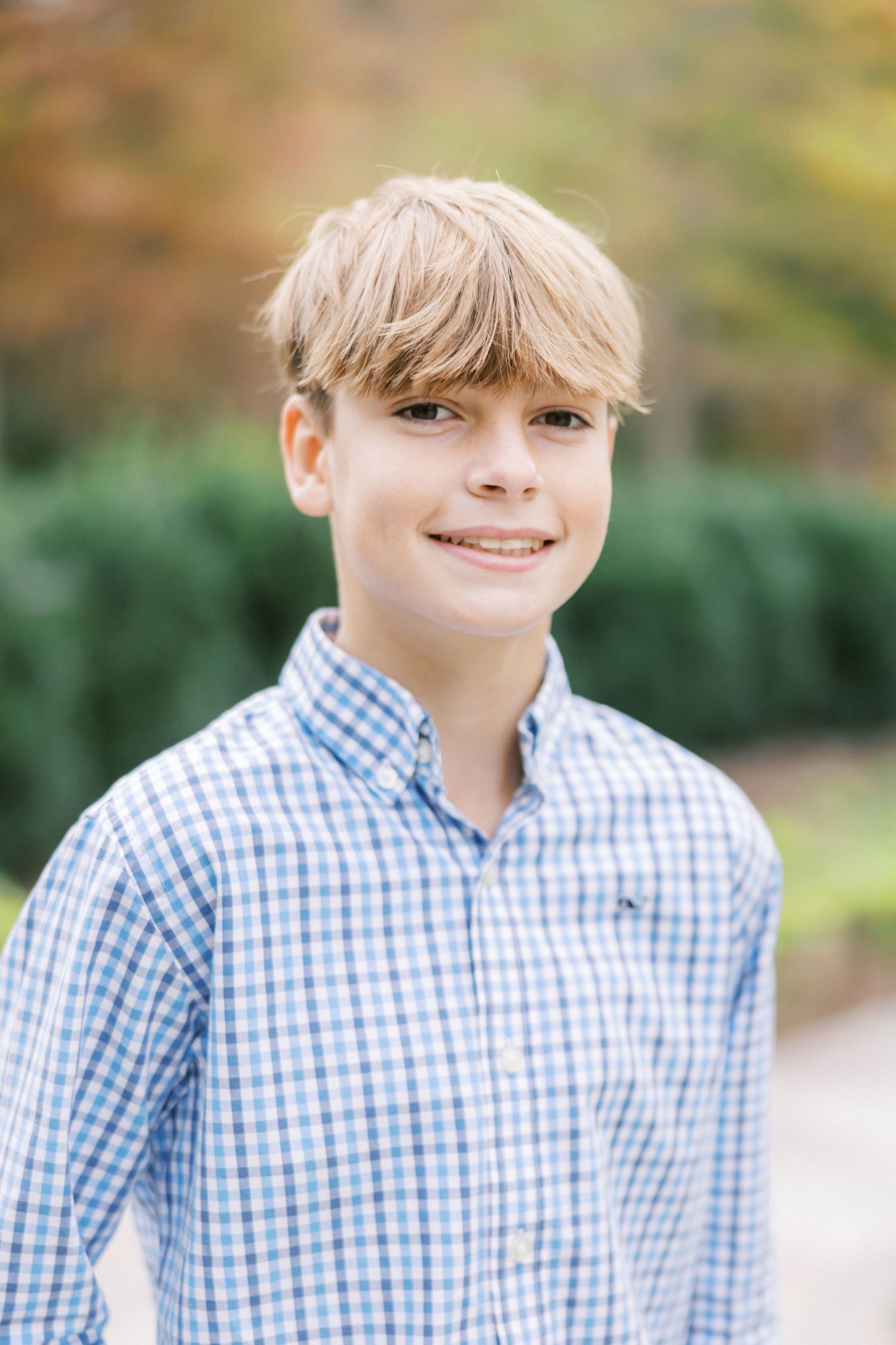 Portrait of a smiling youth with blonde hair wearing a blue and white checkered button-down shirt outdoors.