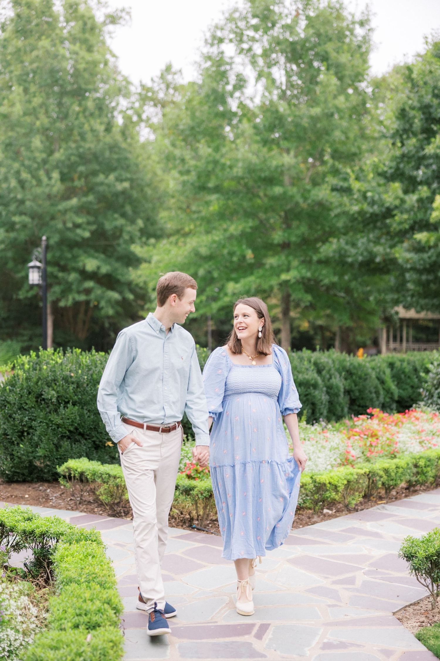 Couple strolls together on stone path through manicured garden with trees in background.