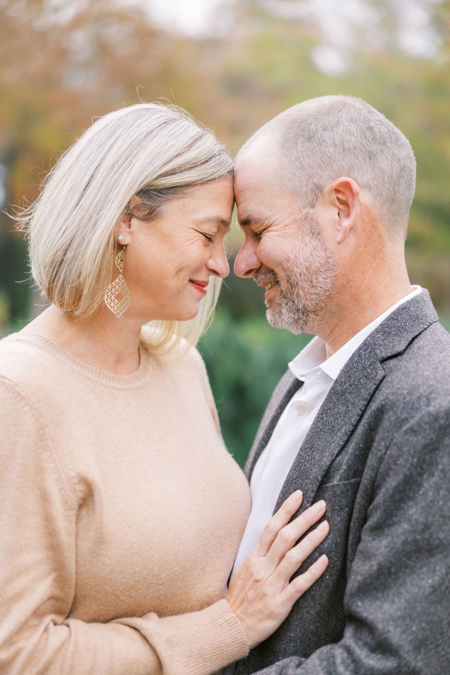 A couple in casual formal wear share an intimate moment together outdoors with soft natural lighting.