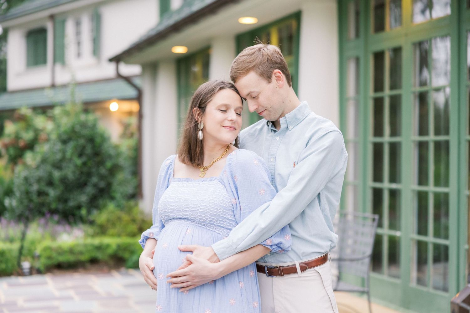 A couple shares a tender moment in front of a house with green trim.