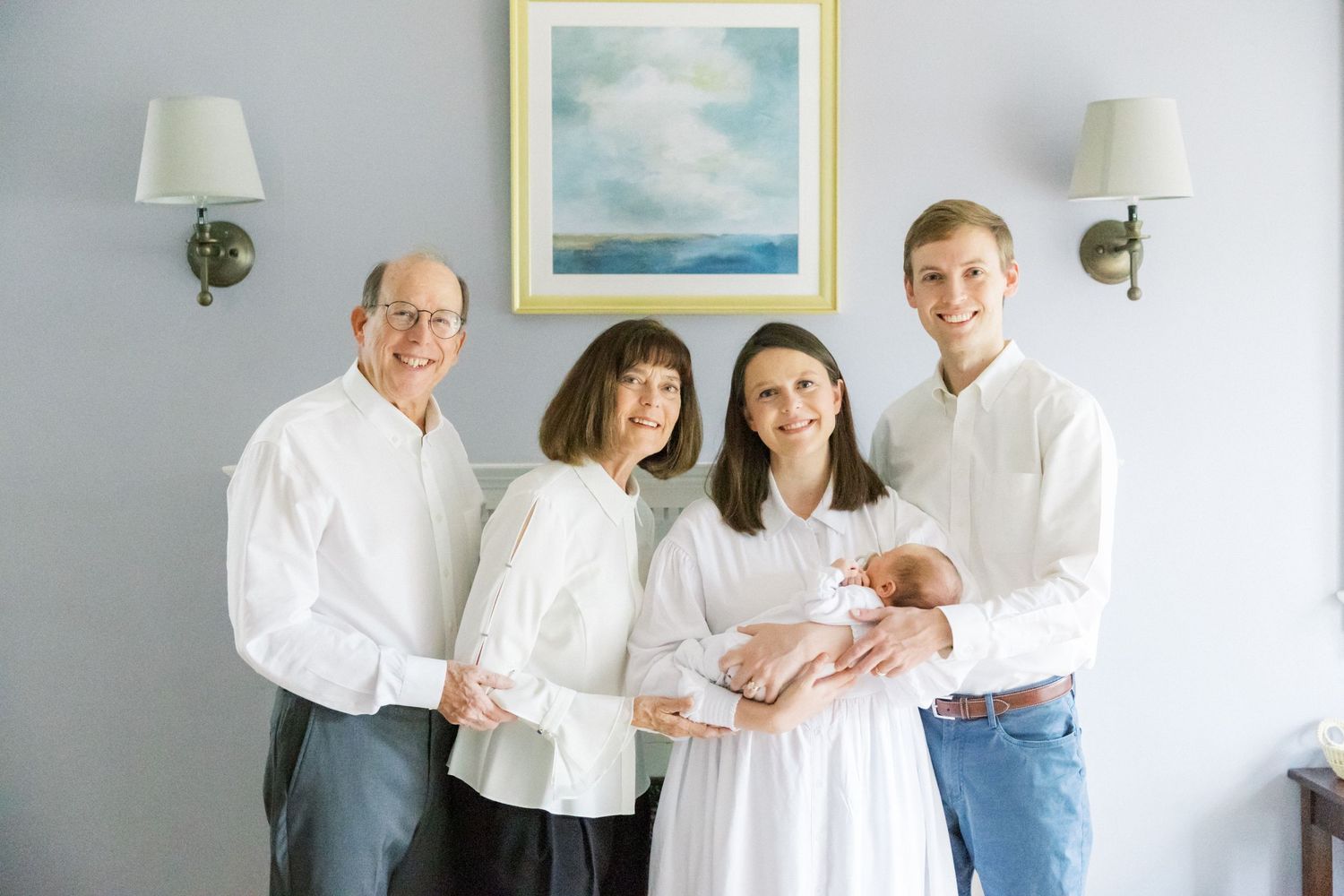 Multi-generational family wearing white poses together with a newborn baby in an elegantly decorated room.