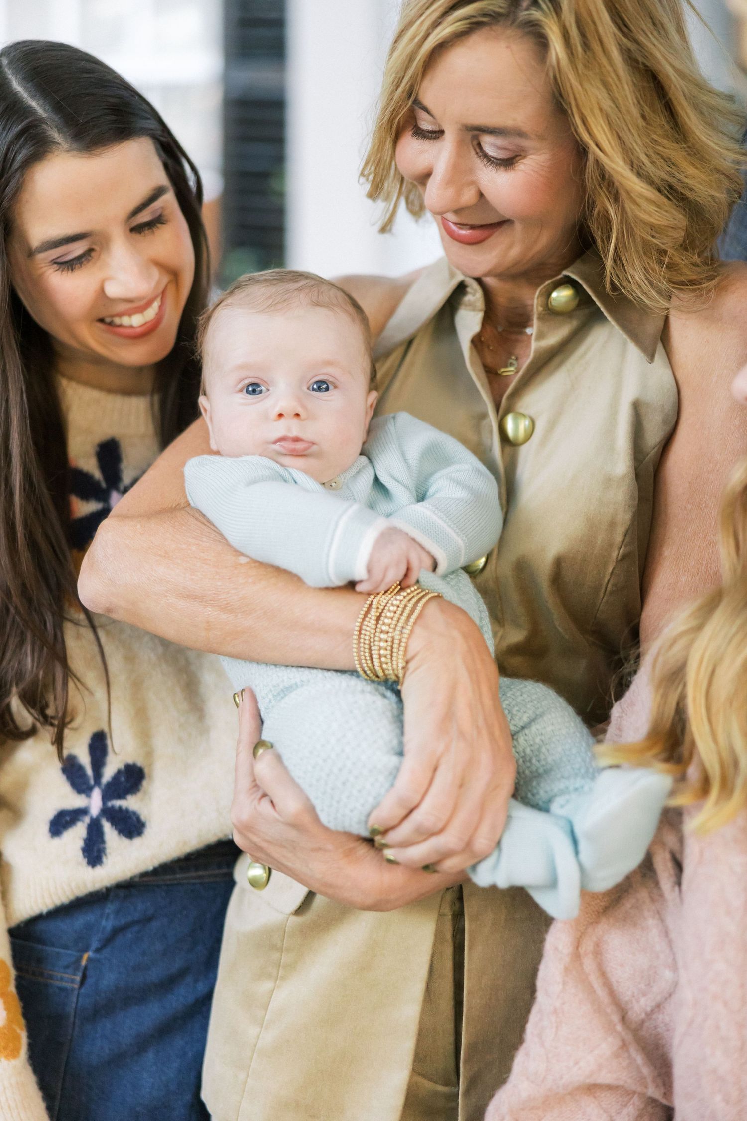 Three people share a joyful moment while holding a baby dressed in light blue.