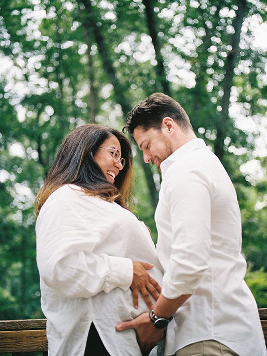 A loving couple in white attire sharing an intimate moment outdoors against a bokeh forest background.