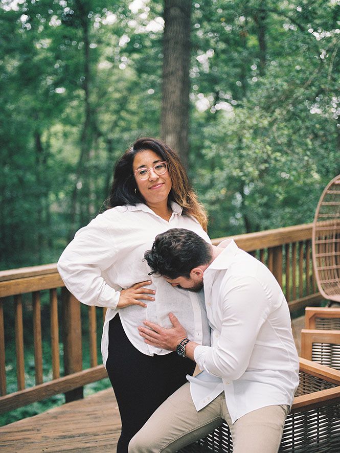A couple shares an intimate moment on a wooden deck with lush forest scenery in the background.
