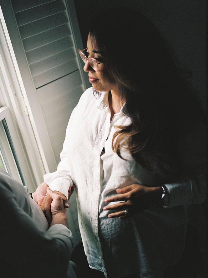 A romantic moment captured in moody lighting near a window with white shutters.