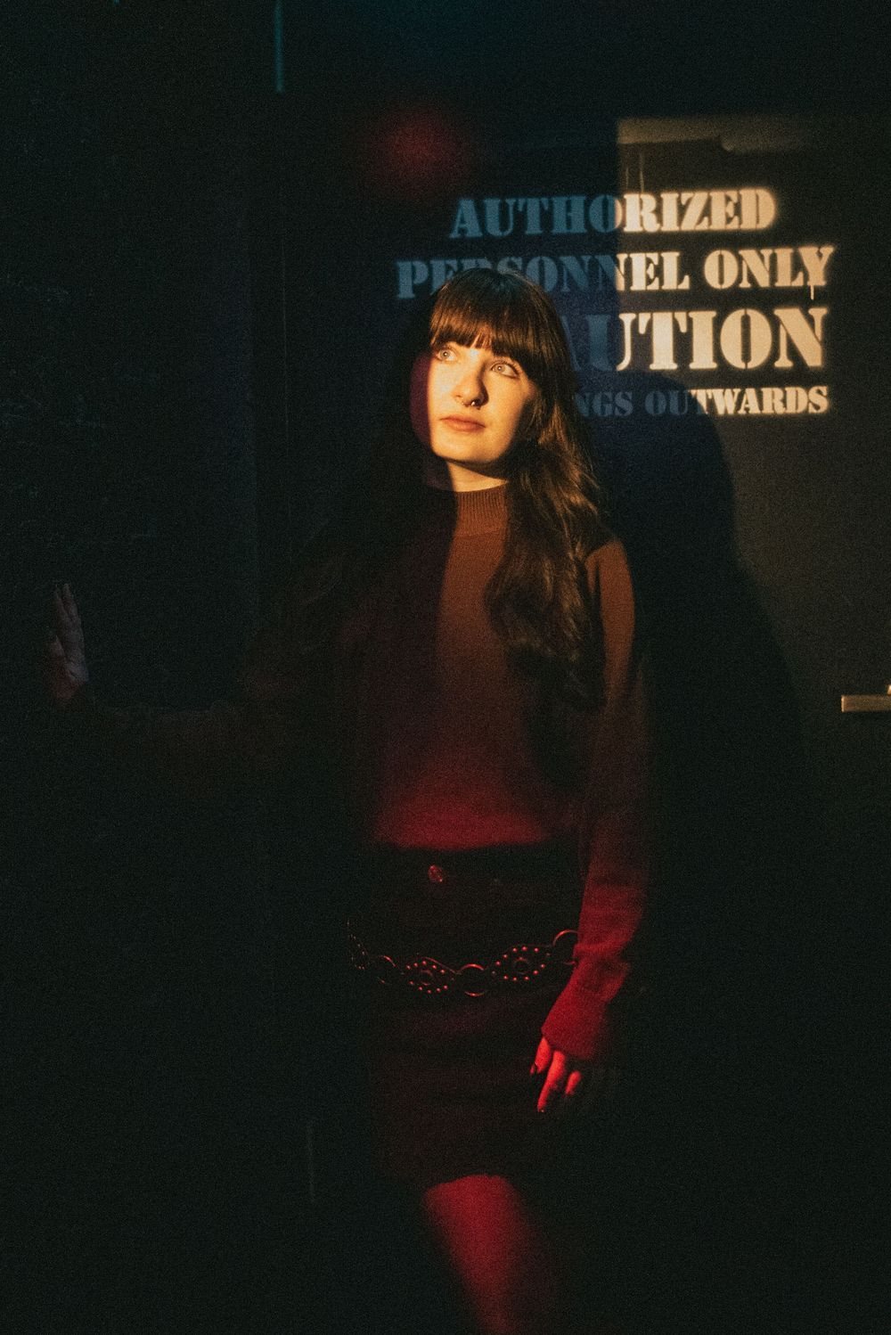 A person stands in a dimly lit area with red lighting near a sign that reads 'Authorized Personnel Only' in moody lighting.