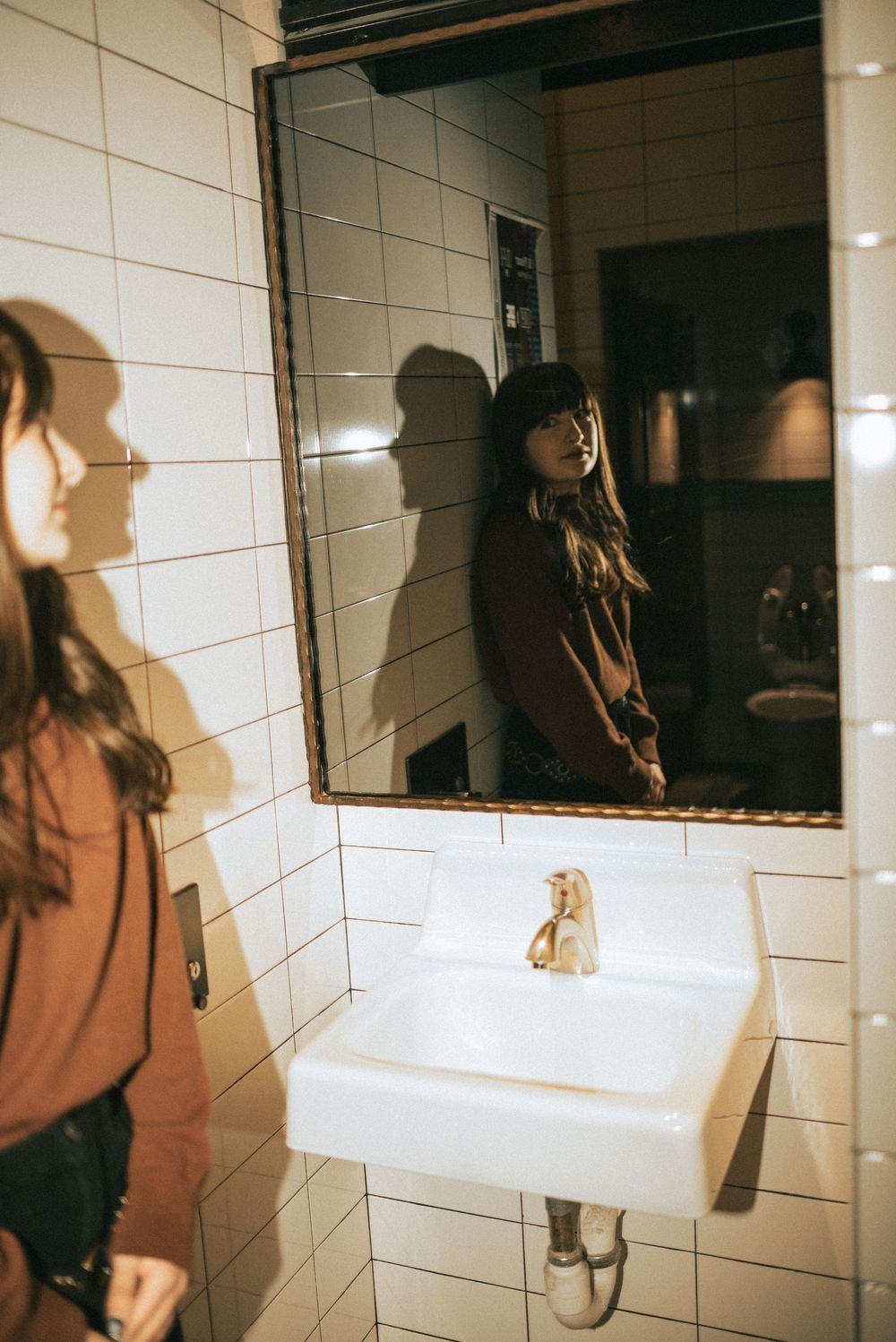 Artistic bathroom mirror reflection shot with white tiled walls and mounted sink in moody lighting.