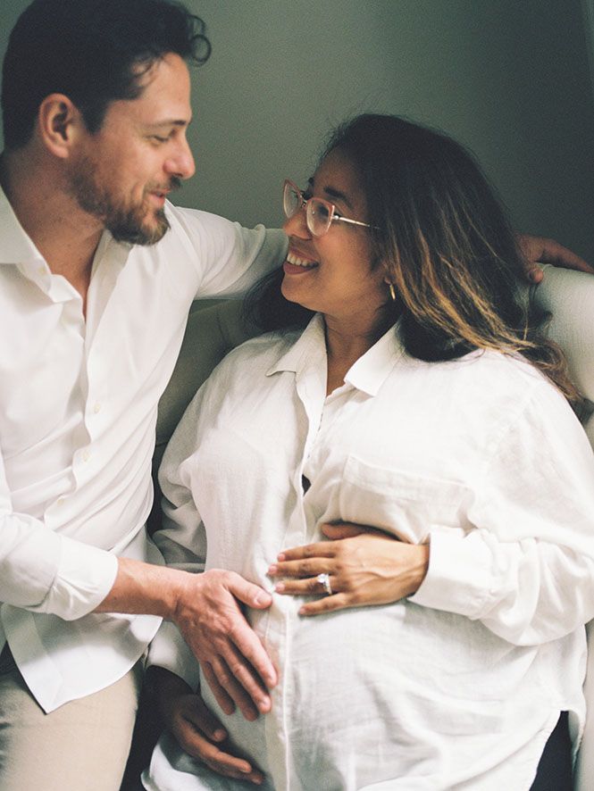 An intimate maternity moment between a couple wearing white shirts as they embrace and smile together.