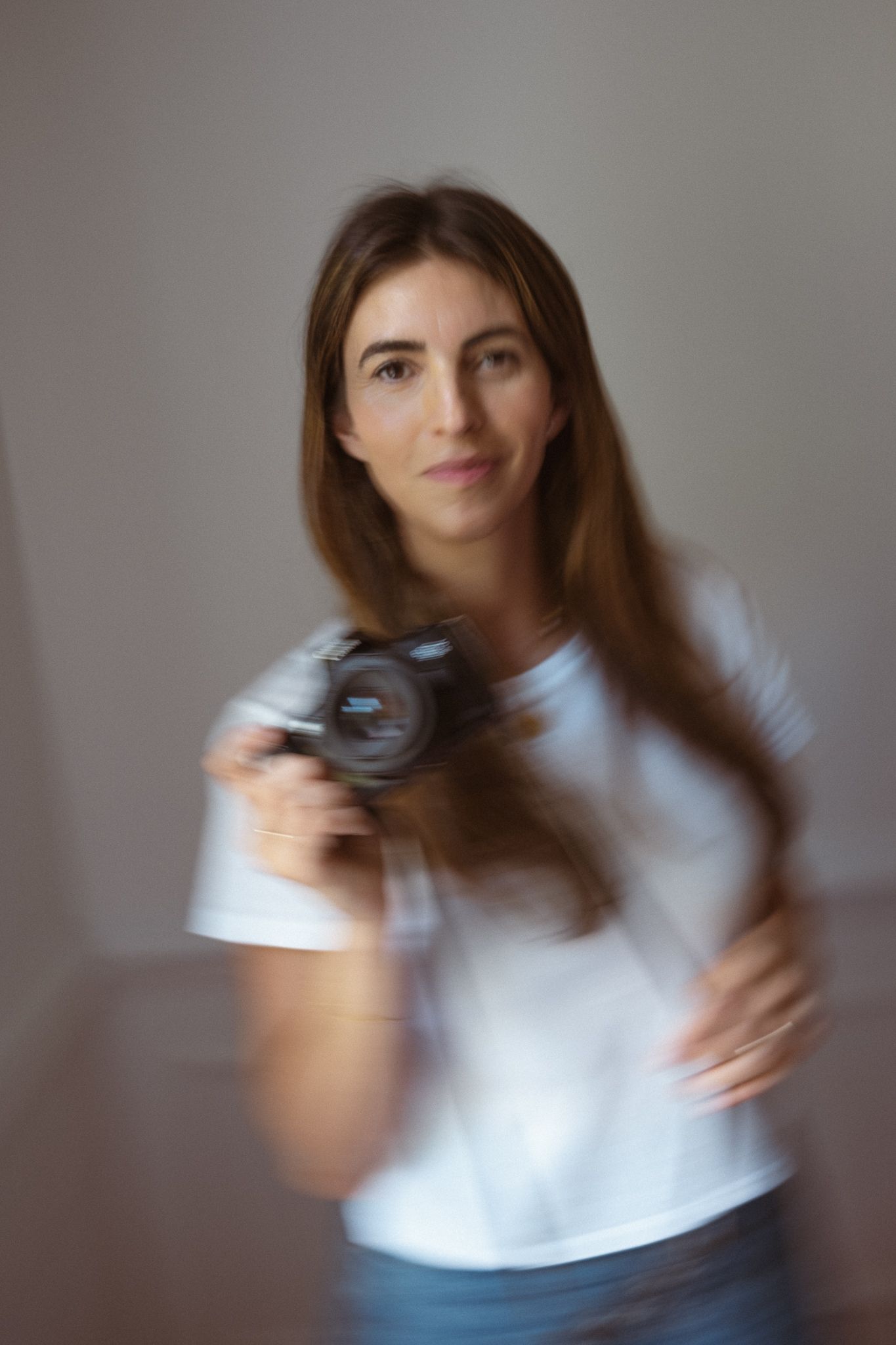Motion-blurred portrait shot of a photographer holding a digital camera while wearing a white t-shirt.