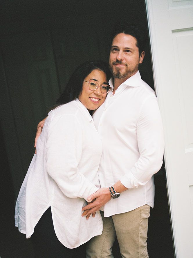 A couple in matching white shirts embraces while standing in a doorway.