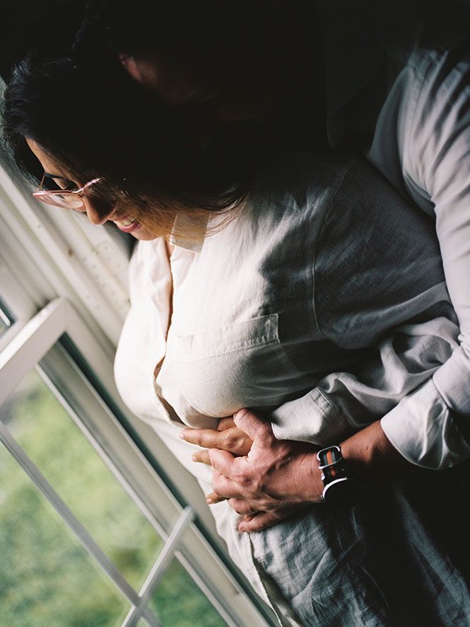 A tender pregnancy portrait showing gentle hands cradling a baby bump by a bright window.