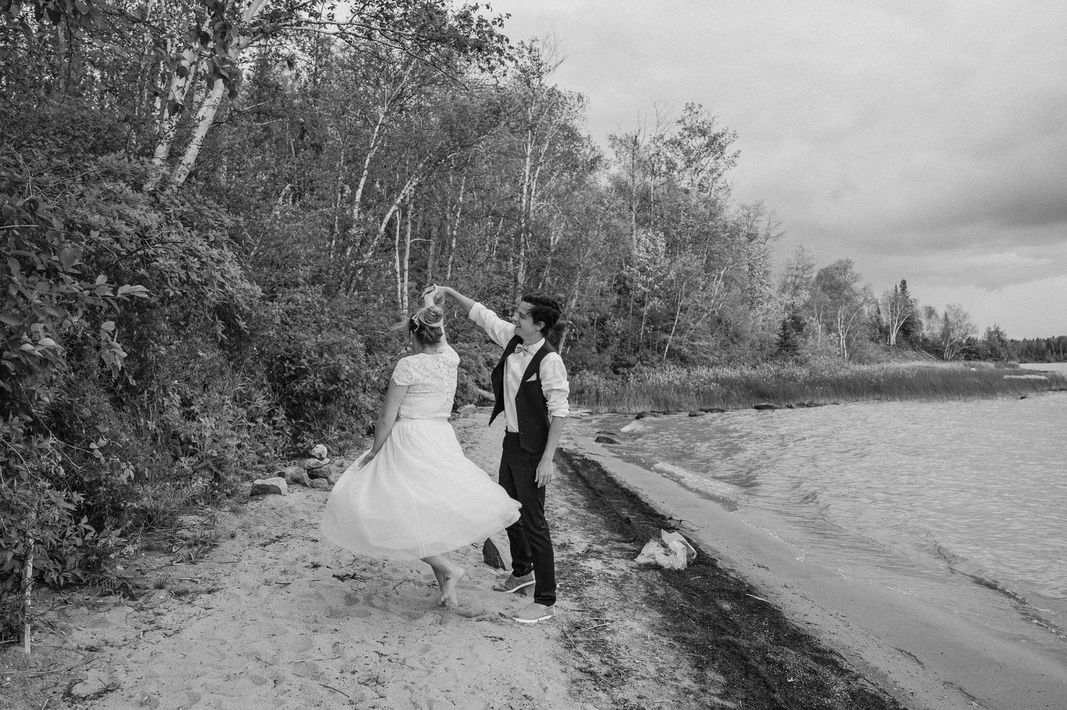 Wedding couple walks along shoreline in black and white photography.