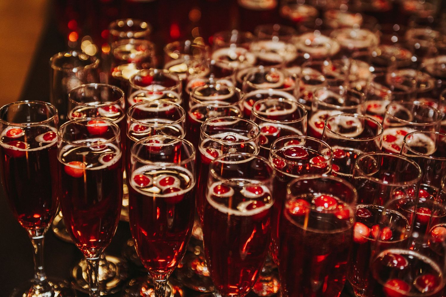 Multiple glasses of red wine arranged in rows on a dark background with dramatic lighting creating a luxurious ambiance.