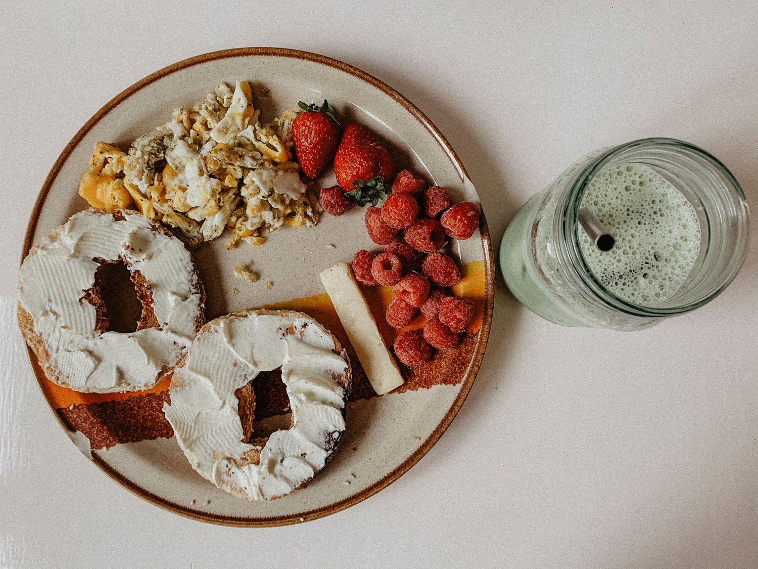 Assiette de petit-déjeuner avec des bagels, des œufs brouillés et des fraises à côté d’un verre de matcha latte.