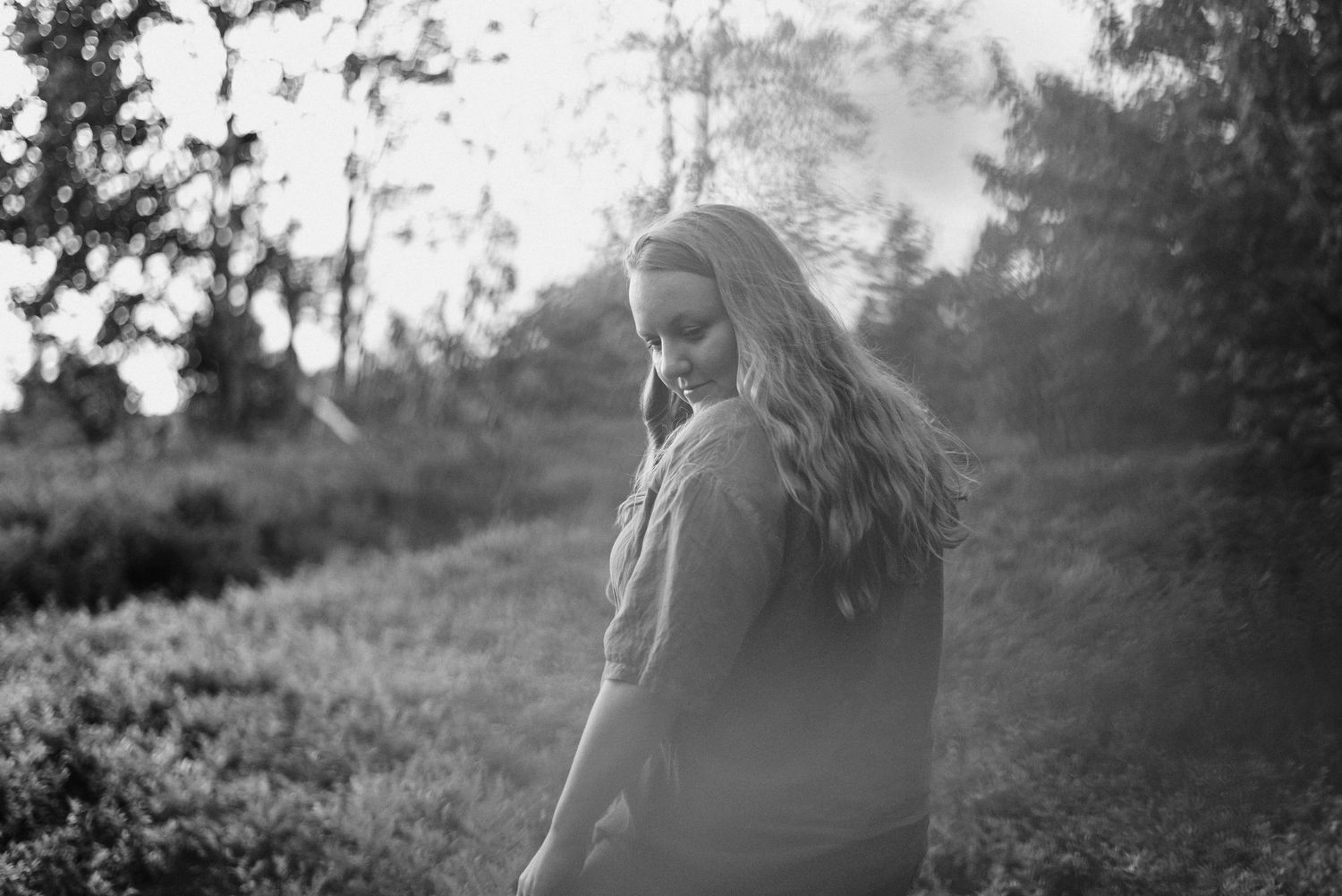 A black and white photo of a person standing in nature with sunlight glowing from behind on a peaceful morning.