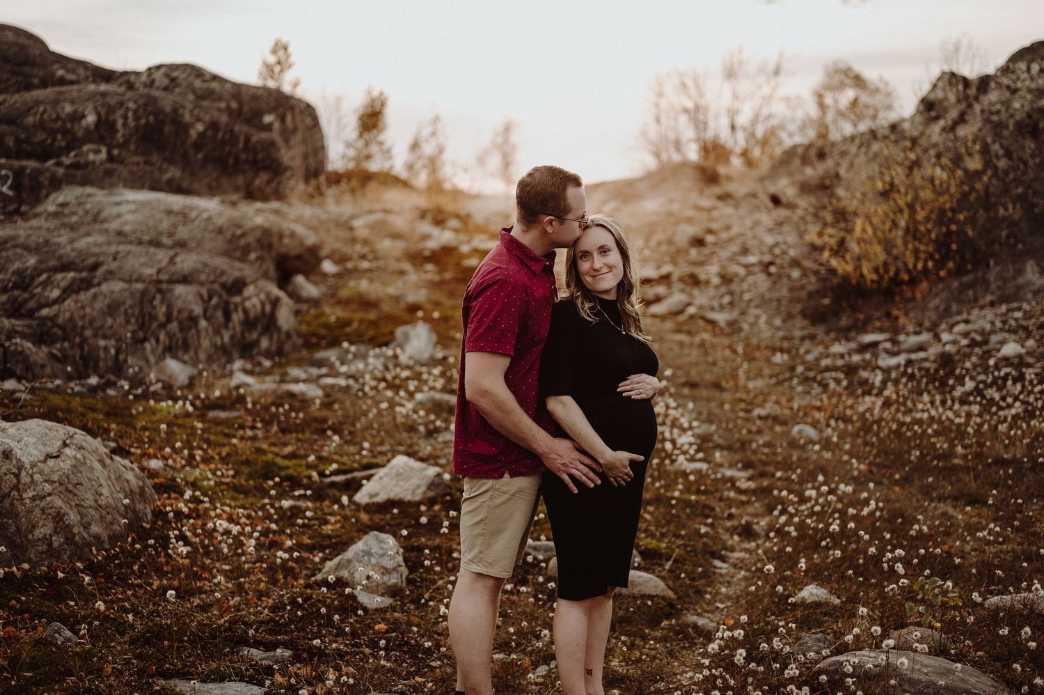 A couple embraces in an autumn field at sunset with warm golden lighting and natural surroundings.