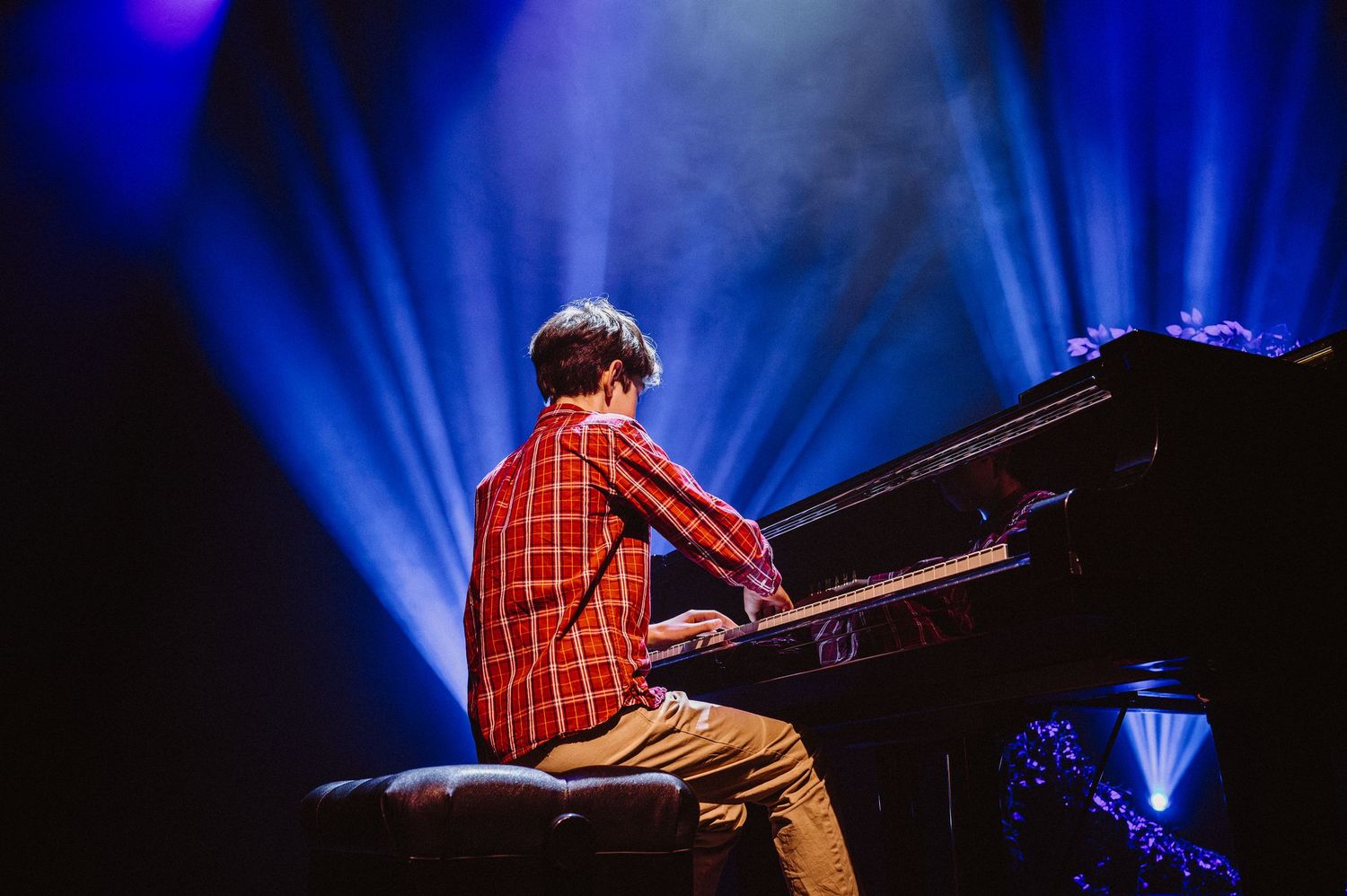 A pianist performs on stage illuminated by dramatic blue spotlights at a concert venue.