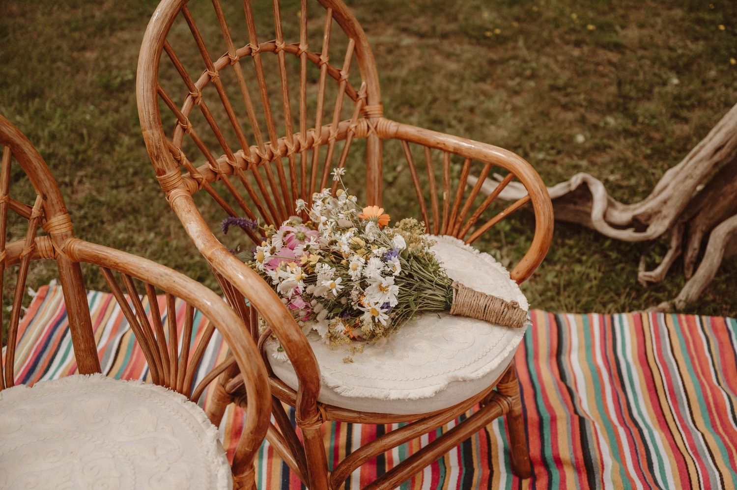 A rustic wedding bouquet rests on a rattan chair with striped cushions.