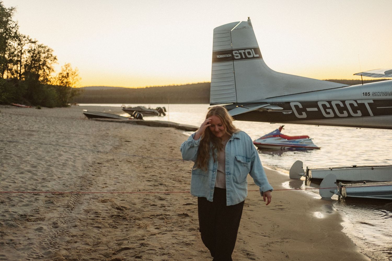 Petit avion stationné au bord de la plage pendant l’heure dorée, avec une personne marchant à proximité.