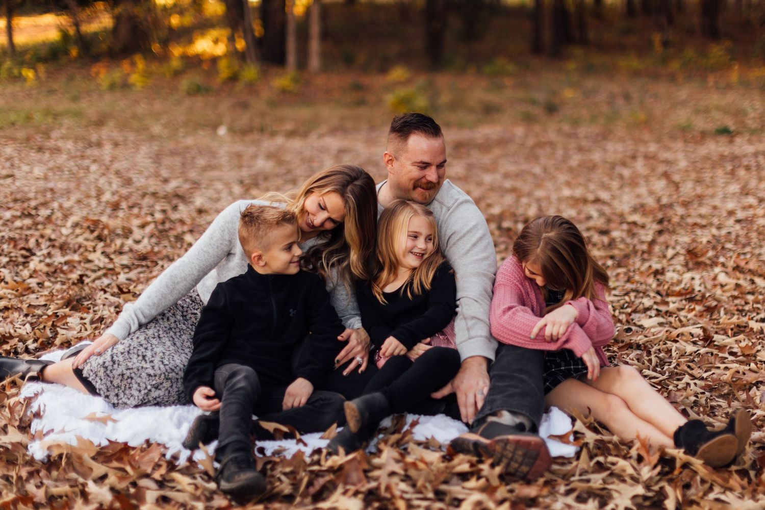 Family sitting together on blanket in autumn leaves.
