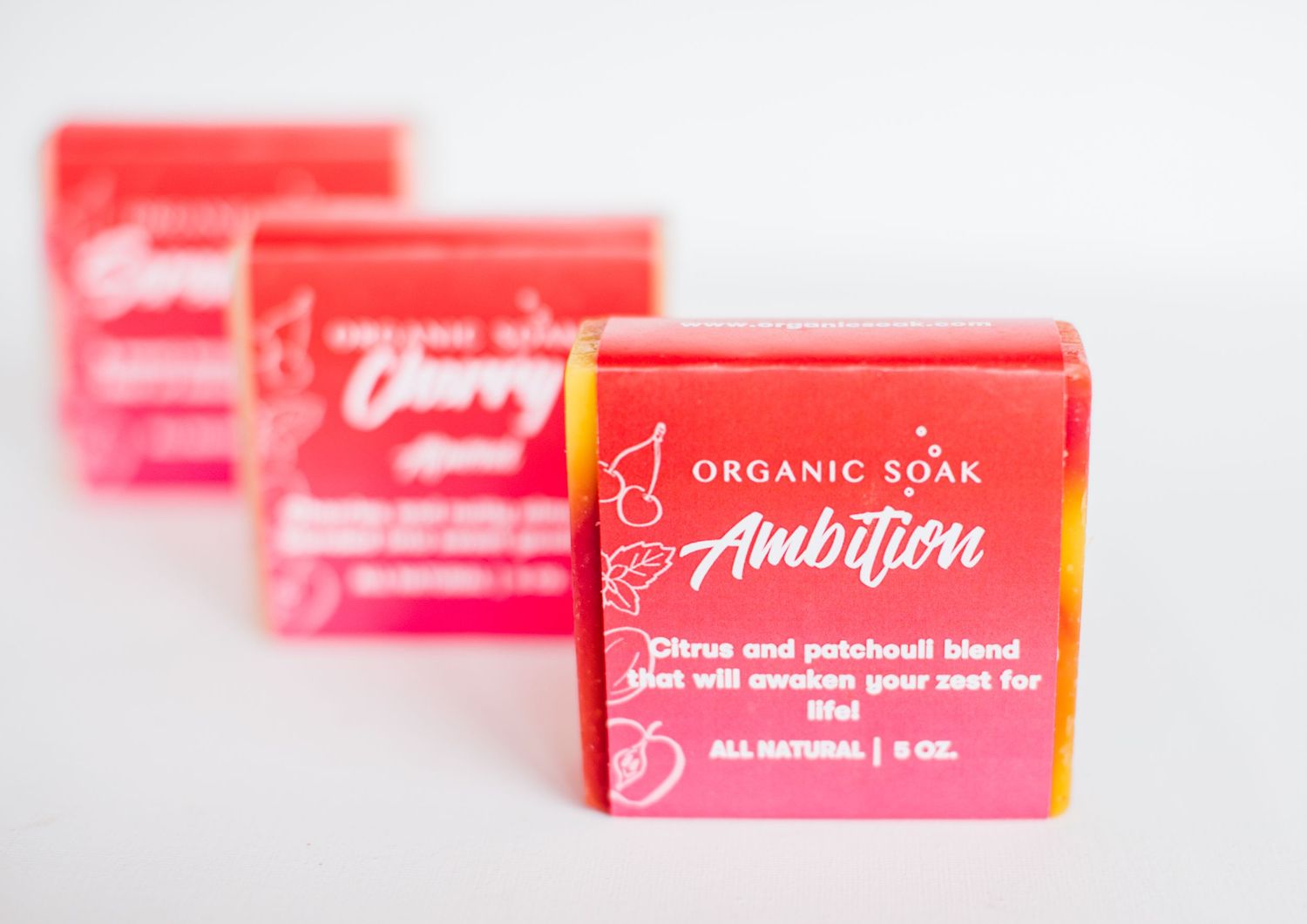 Three pink boxes of organic 'Ambition' soap arranged in a row on a white surface showing minimalist product packaging.