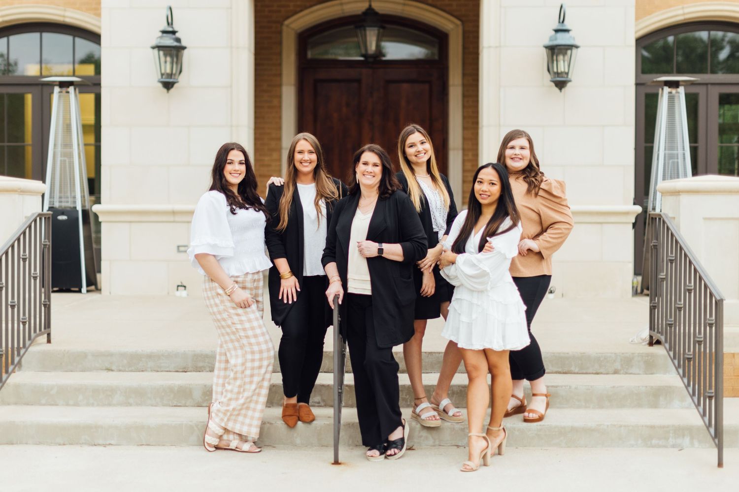 A group in formal attire poses together at the entrance of a stone building.