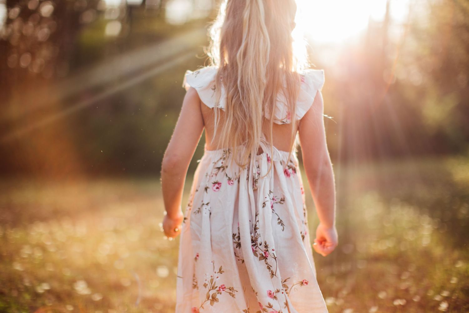 A person wearing a floral white dress walks through a sun-drenched garden with glowing golden bokeh light effects.