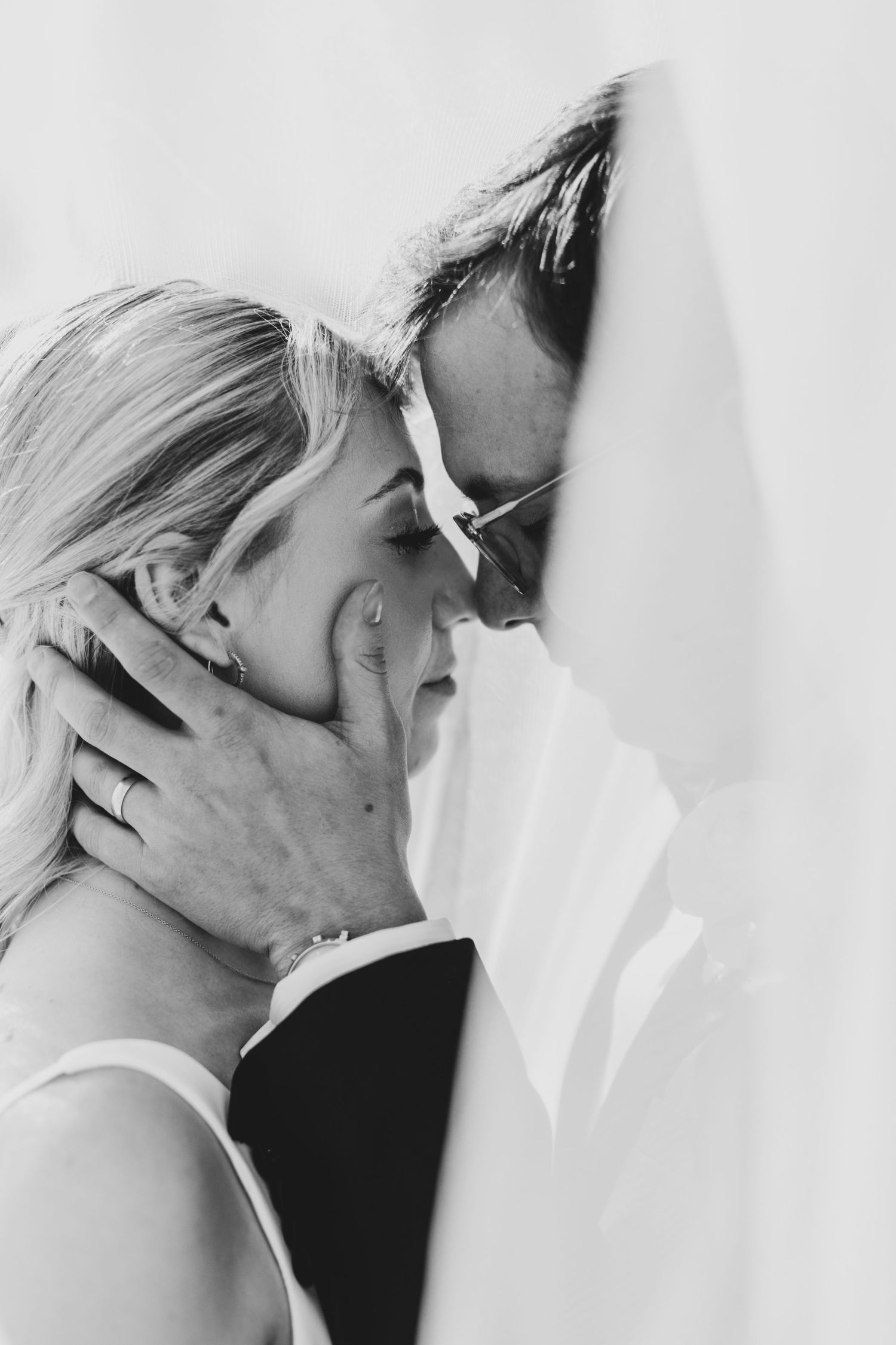 Romantic black and white close-up captures intimate moment through delicate white veil.