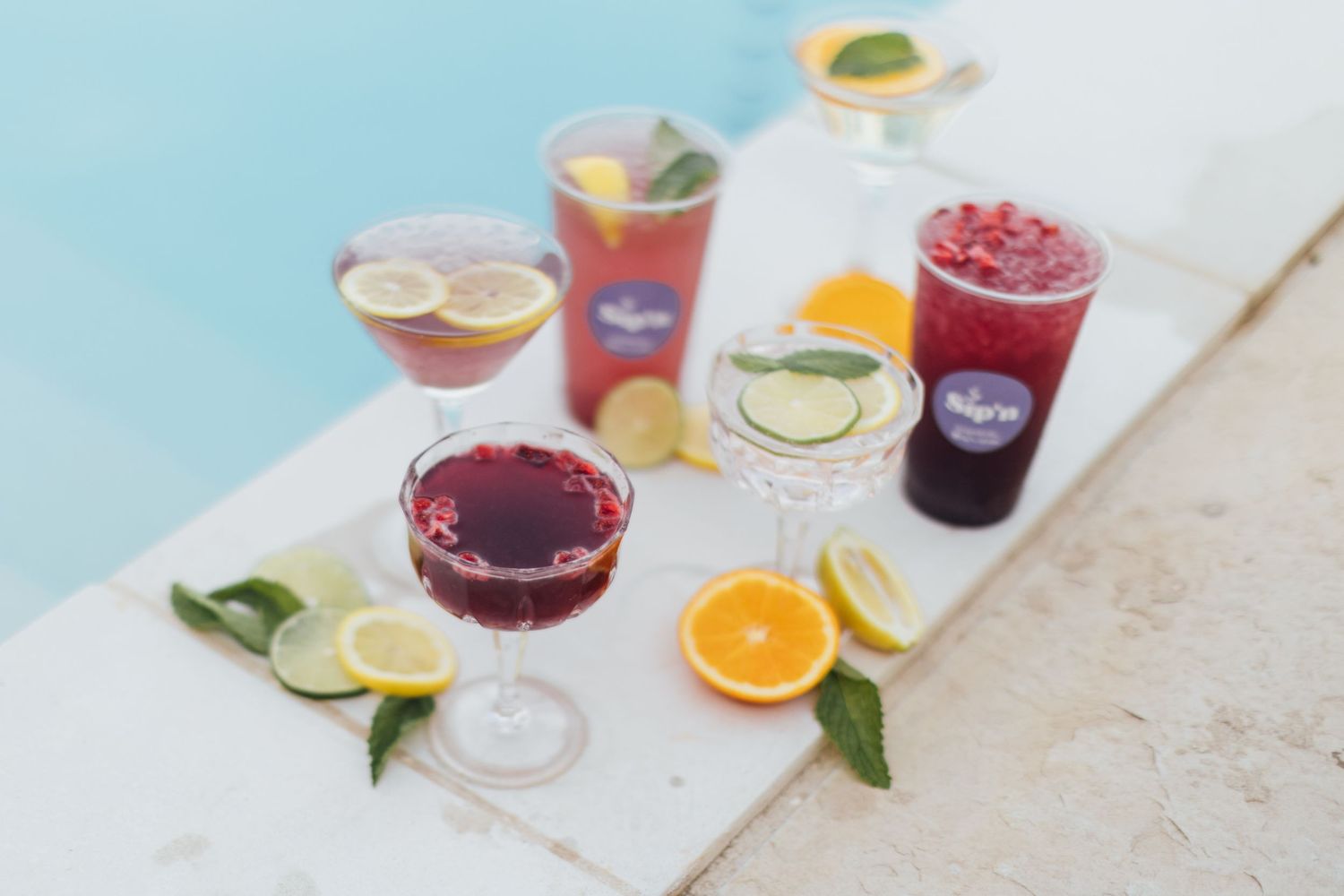 Colorful summer cocktails with citrus garnishes arranged on a white surface against a light blue background.