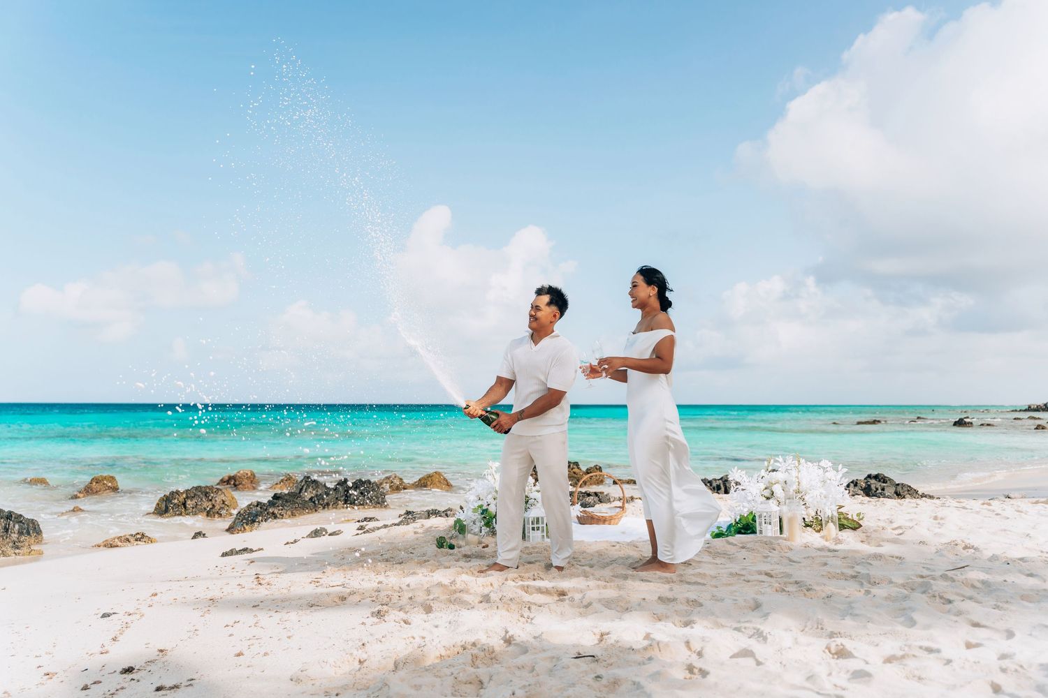 Couple stands on tropical beach with turquoise water and white sand during romantic ceremony at shoreline.