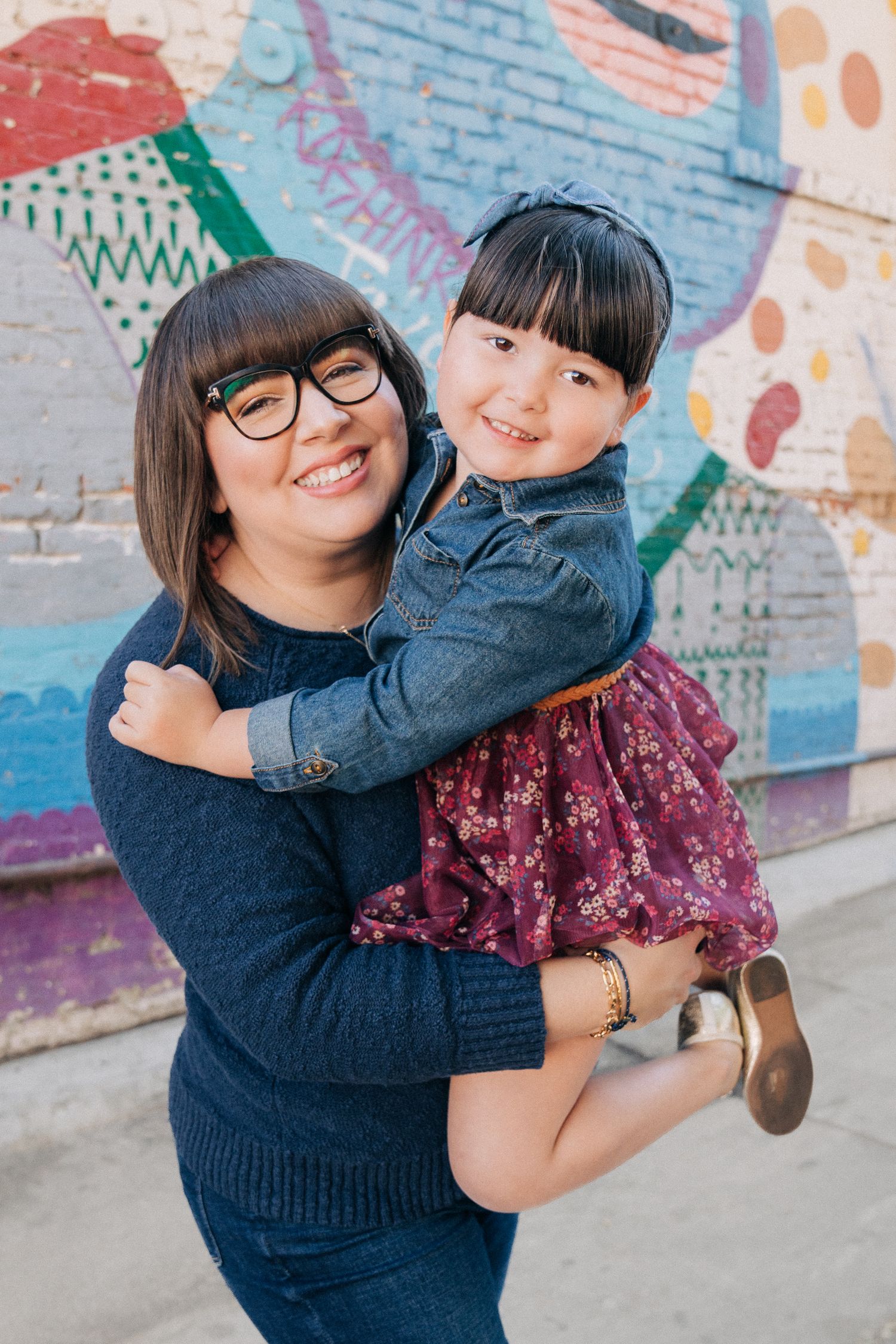 Two people embrace and smile playfully in front of a colorful graffiti wall.