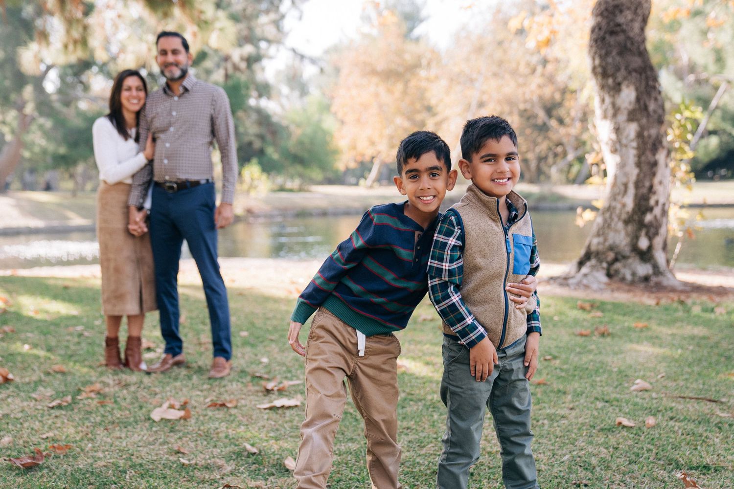 A series of candid outdoor family portraits taken in warm autumn light at a park with fallen leaves scattered on the ground.