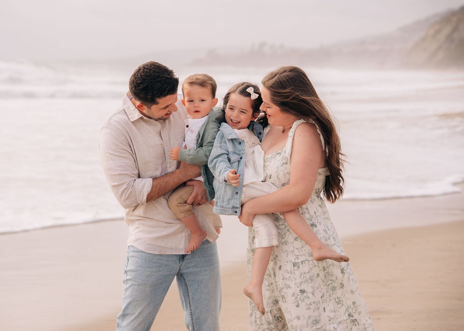 A family shares a joyful moment together while walking along a misty beach at sunset.