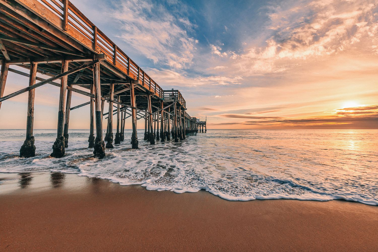 Dramatic sunset over a wooden pier stretches into the ocean as golden light reflects off calm waters.